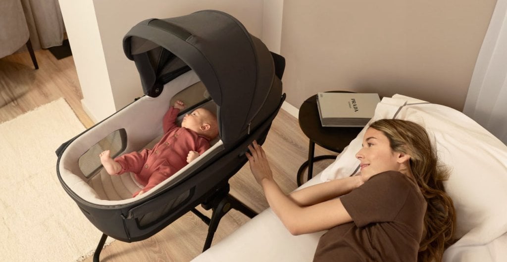 Maman allongée veillant son bébé dans la nacelle Inglesina posée sur son stand, poussette évolutive utilisable comme berceau à la maison