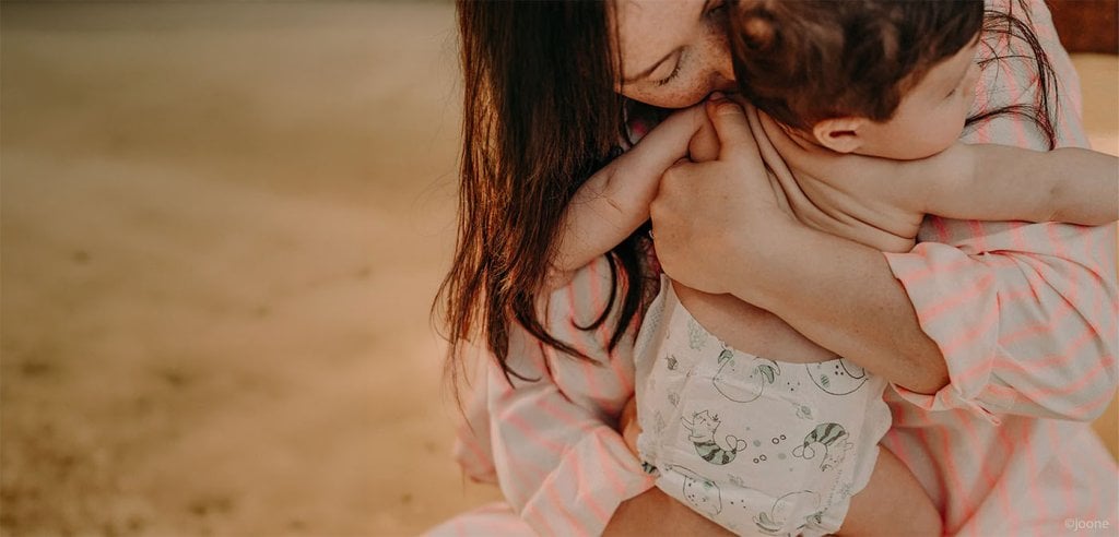 Maman serrant tendrement son bébé sur la plage, conseils pour protéger bébé du soleil et de la chaleur estivale