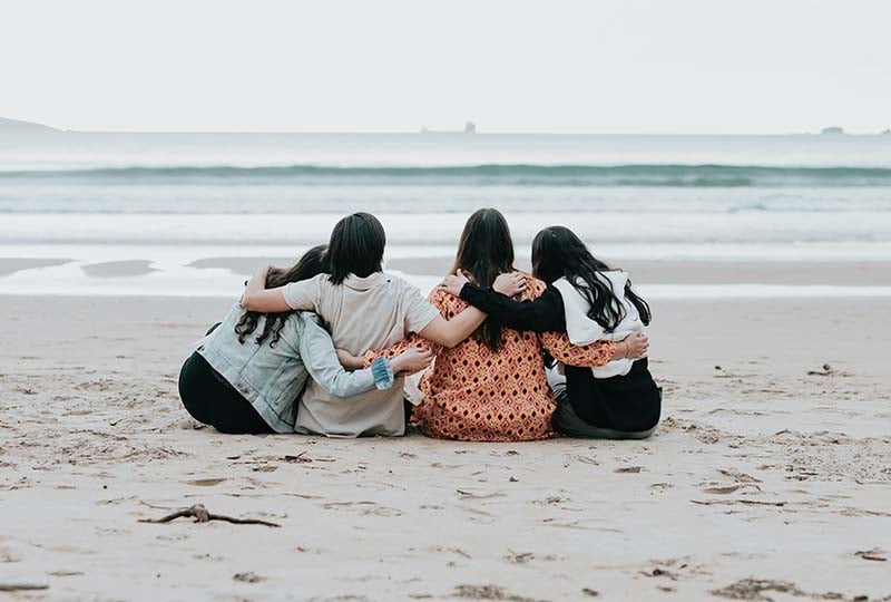 Meilleures idées d'EVJF avec une femme enceinte avant mariage : amies se prenant dans les bras sur la plage. Activités d'EVJF idéales pour se rapprocher et profiter de la nature.