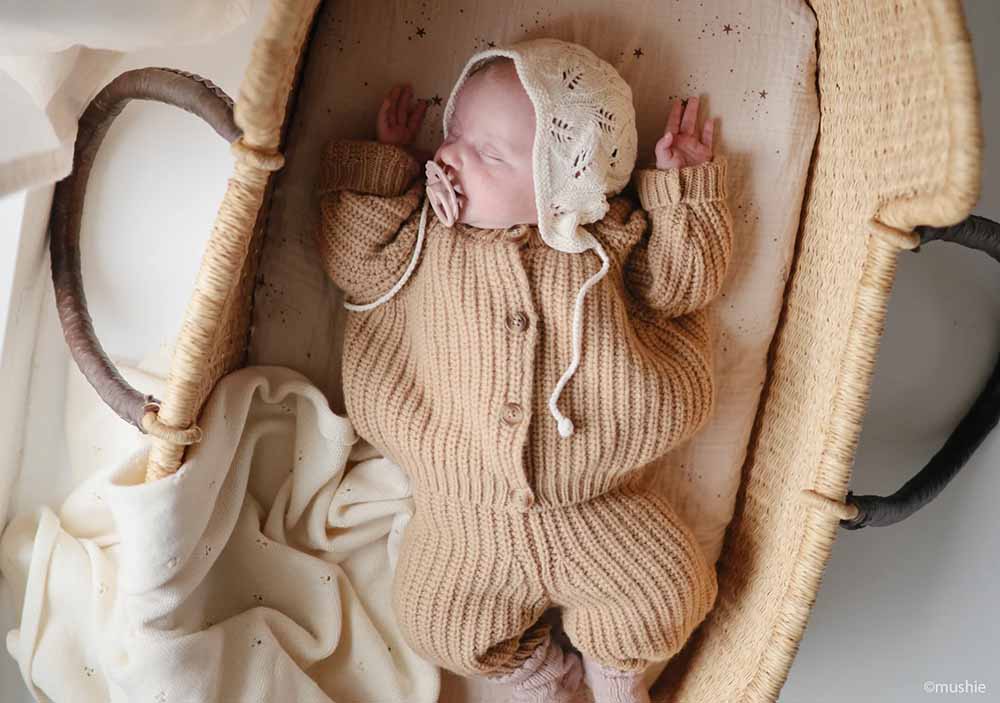 Nouveau-né endormi dans un panier vintage sur fond beige, préparation à l'inscription en maternité, bébé en tenue tricotée beige, idéal pour rechercher des conseils sur l'inscription à la maternité et l'accouchement naturel.