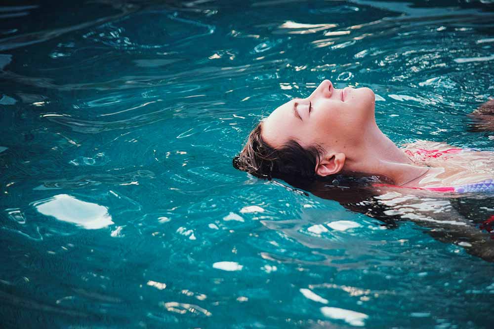 Femme enceinte flottant dans une piscine, préparation à la naissance en milieu aquatique. Pourquoi choisir une séance préparation naissance accouchement bébé en piscine pour détendre le corps ?