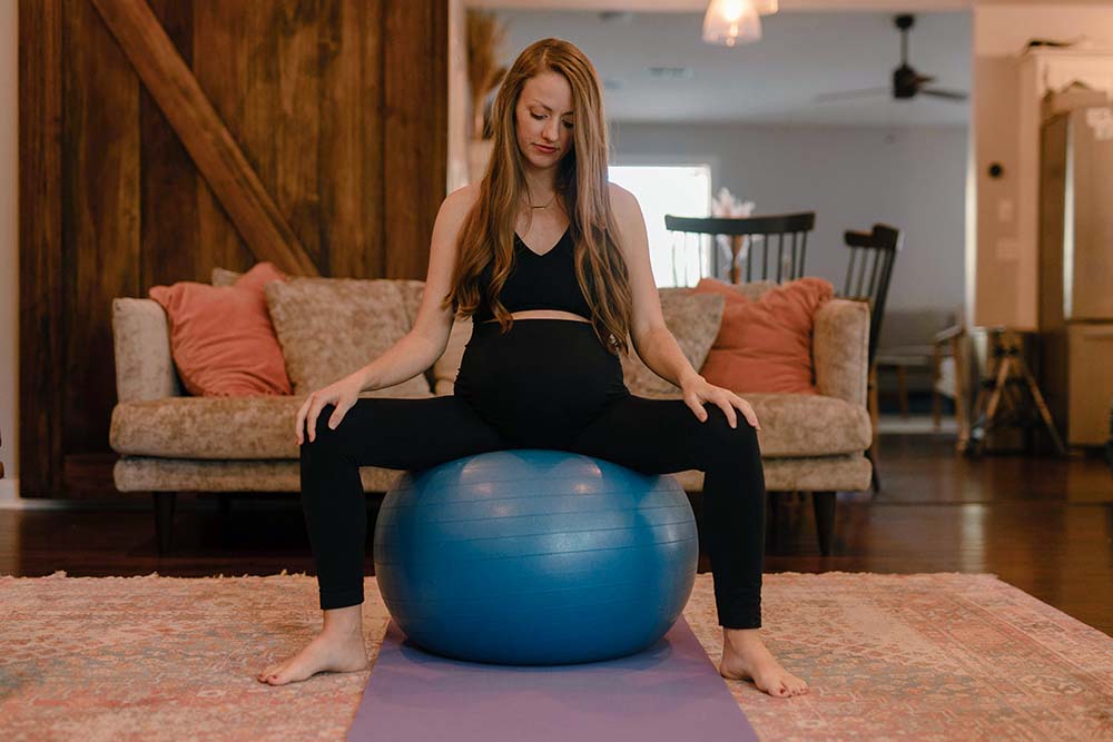 Femme enceinte assise sur un ballon d'exercice pour la préparation à l'accouchement. Quels exercices faire à la maison pour une séance préparation naissance accouchement bébé avec un ballon ?