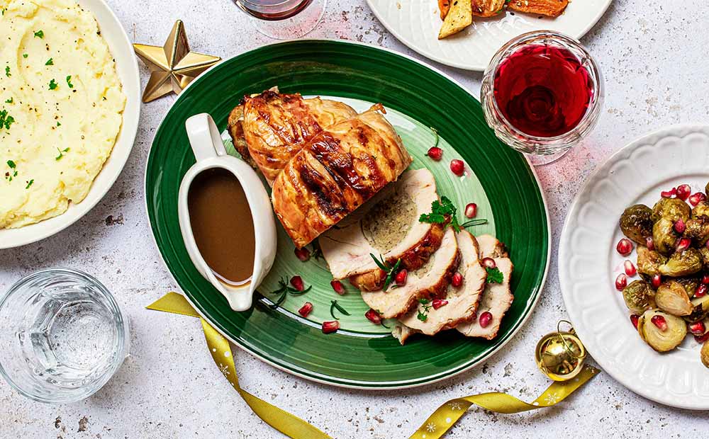 Que manger à Noël enceinte viande rôtie : plat principal de Noël pour femme enceinte : viande rôtie tranchée, accompagnée de sauce et de grenades sur une table festive. Idées de plats de Noël adaptés à la grossesse sans danger.