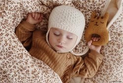 Bébé garçon endormi avec un bonnet en laine et une peluche, illustrant les prénoms anciens et beaux pour garçon. Parfait pour les recherches sur les vieux prénoms de garçon vintage et rétro en 2024. Liste de prénoms.
