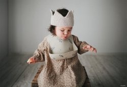 Petite fille portant une couronne en tricot et un bavoir, symbolisant les prénoms anciens pour fille. Idéal pour les recherches sur les prénoms de fille vintage et rétro. Liste de prénoms.