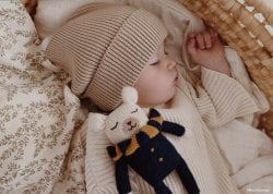 Bébé garçon endormi en bonnet et pull beige, tenant une peluche, symbolisant les tendances des top prénoms garçon 2024. Idéal pour les recherches sur les prénoms masculins populaires, les prénoms à la mode pour bébés garçons, et les prénoms tendance pour garçons en 2024.