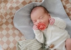 Photo d'un nouveau-né endormi avec une tétine rose. Découvrez les top prénoms fille tendance 2024 pour votre future petite princesse. Liste des plus beaux prénoms féminins pour 2024.